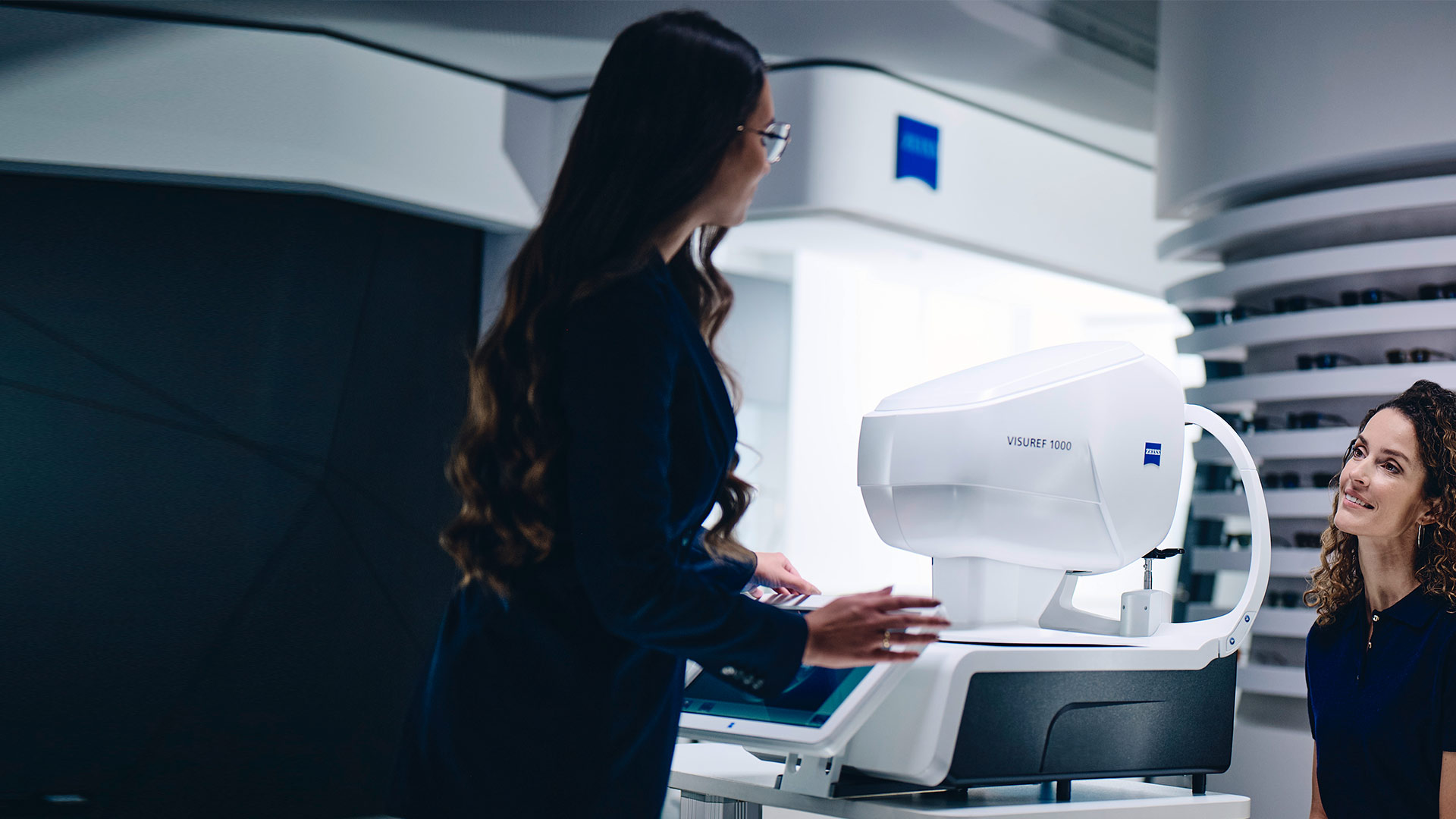 En kvinna sitter framför ZEISS VISUREF 1000 och tittar mot en kvinnlig optiker.