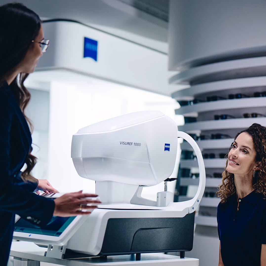 En kvinna sitter framför ZEISS VISUREF 1000 och tittar mot en kvinnlig optiker.