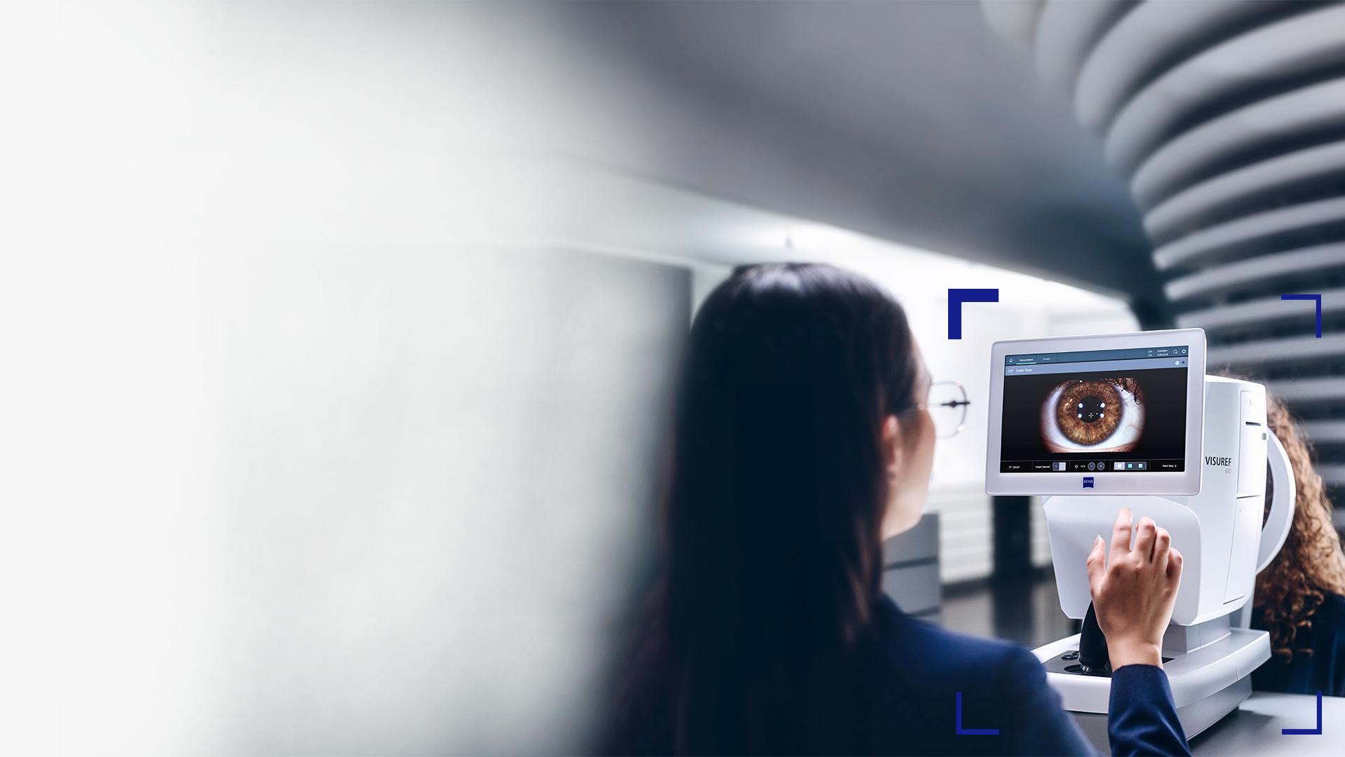 En kvinnlig optiker tittar på skärmen för ZEISS VISUREF 600, där en bild av ett öga visas.