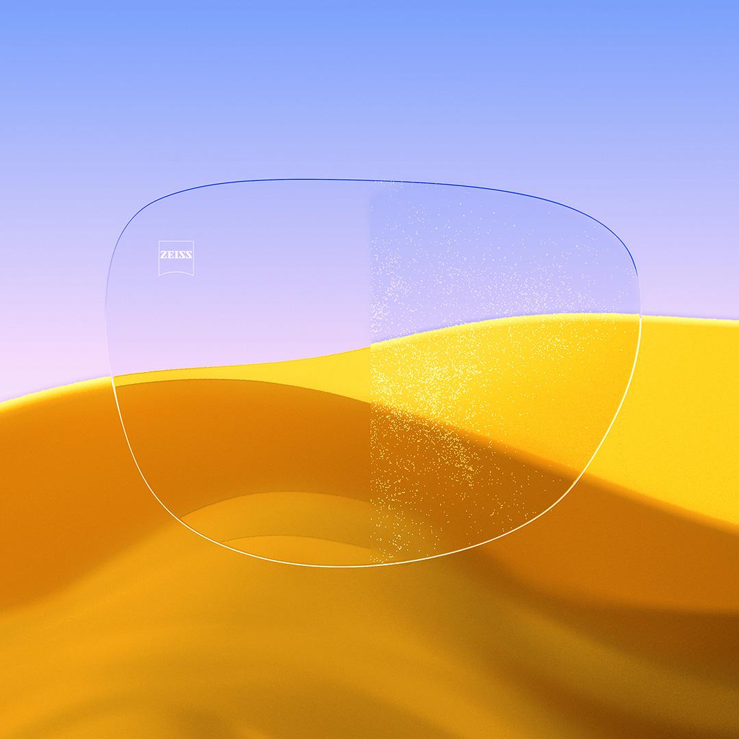 Ett delat glasögonglas där ena sidan, med ZEISS DuraVision Gold UV, är klar och ren, och den andra sidan av glaset är täckt av damm.