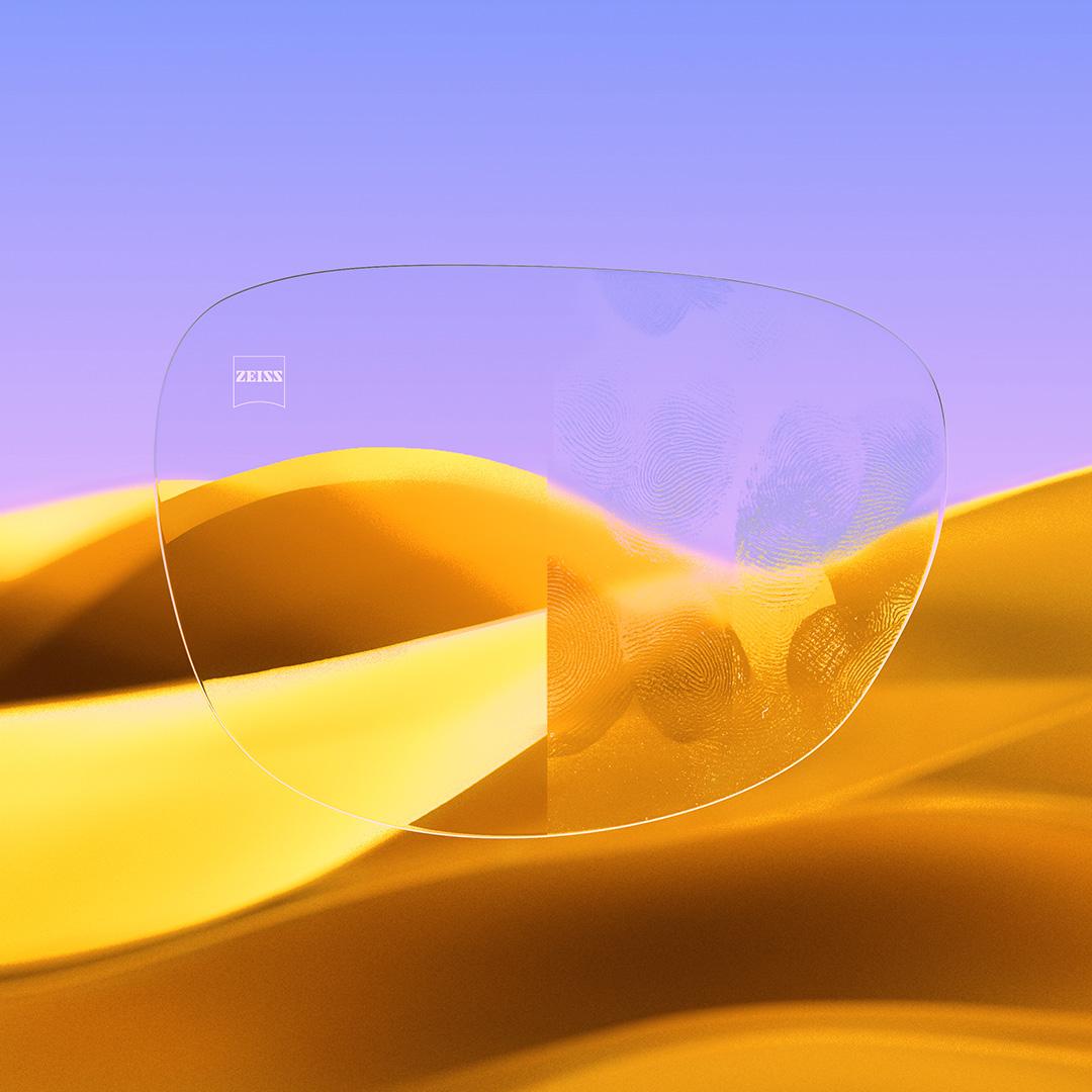 Ett delat glasögonglas där ena sidan, med ZEISS DuraVision Gold UV, är klar och ren, och den andra sidan av glaset är täckt av fingeravtryck.