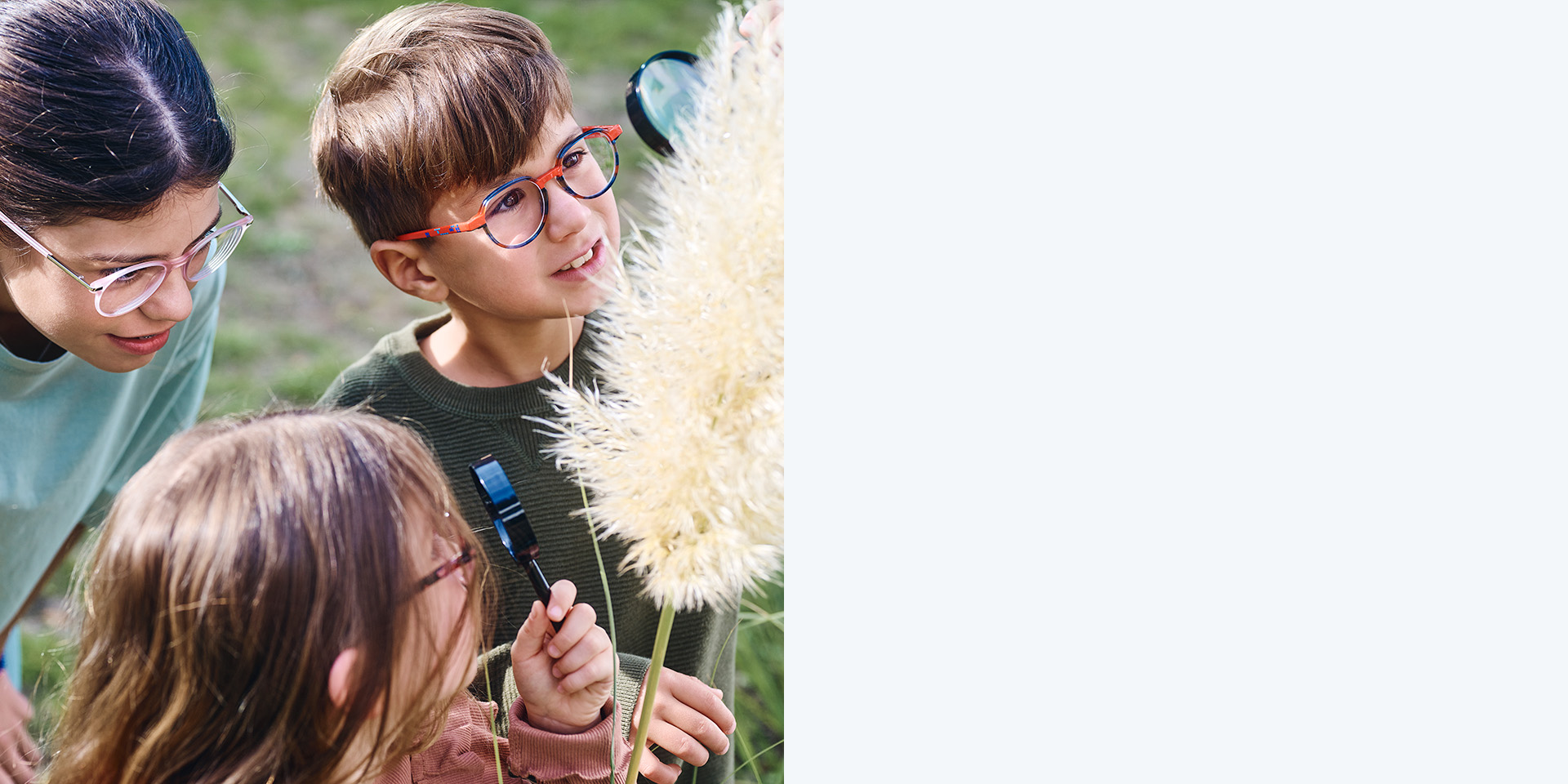 Två flickor och en pojke som bär ZEISS MyoCare-glas. De tittar på en växt, två av de tre barnen tittar på växten genom förstoringsglas.