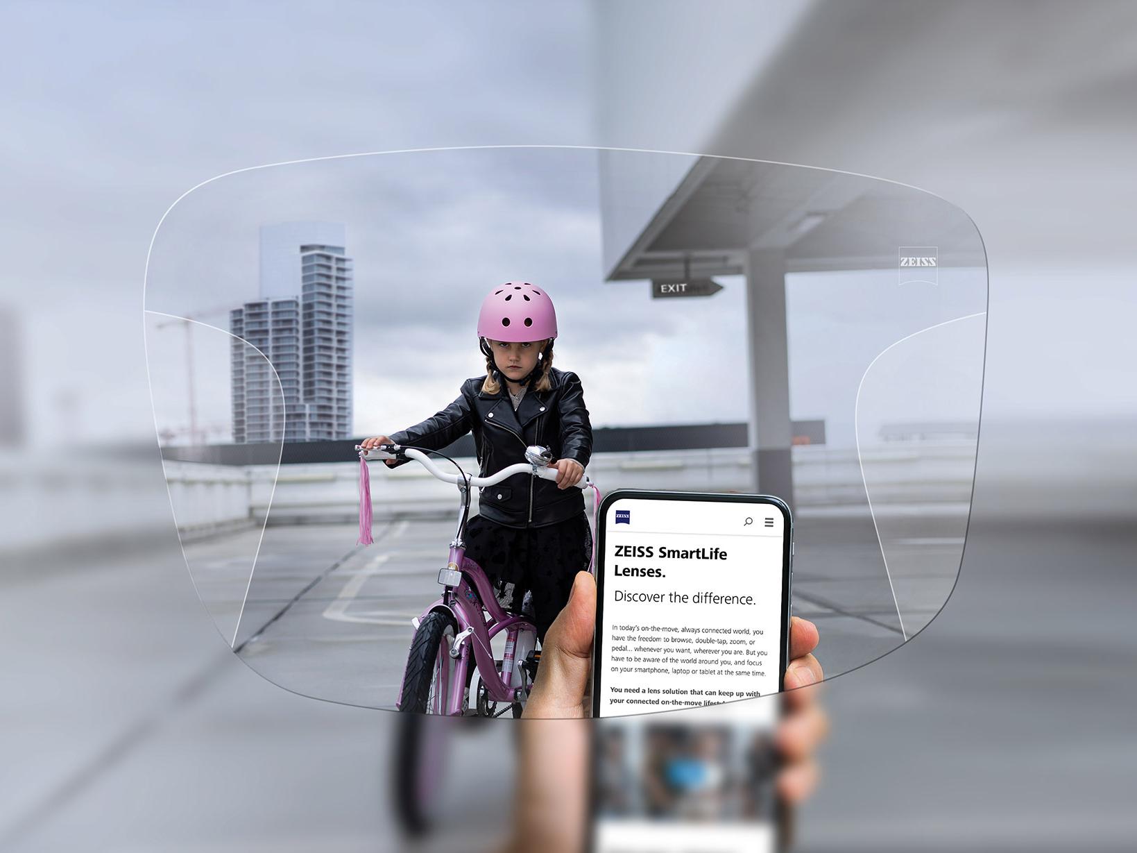 Person tittar på sin telefon genom ZEISS SmartLife progressiva glas. I bakgrunden ser man en flicka på sin cykel som har på sig en rosa cykelhjälm. 