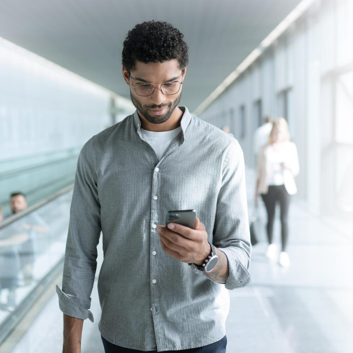 Ung man med ZEISS SmartLife-glasögon tittar på sin telefon under en promenad.