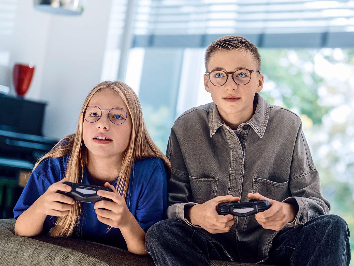 En flicka och en pojke i tonåren spelar videospel på konsoler.