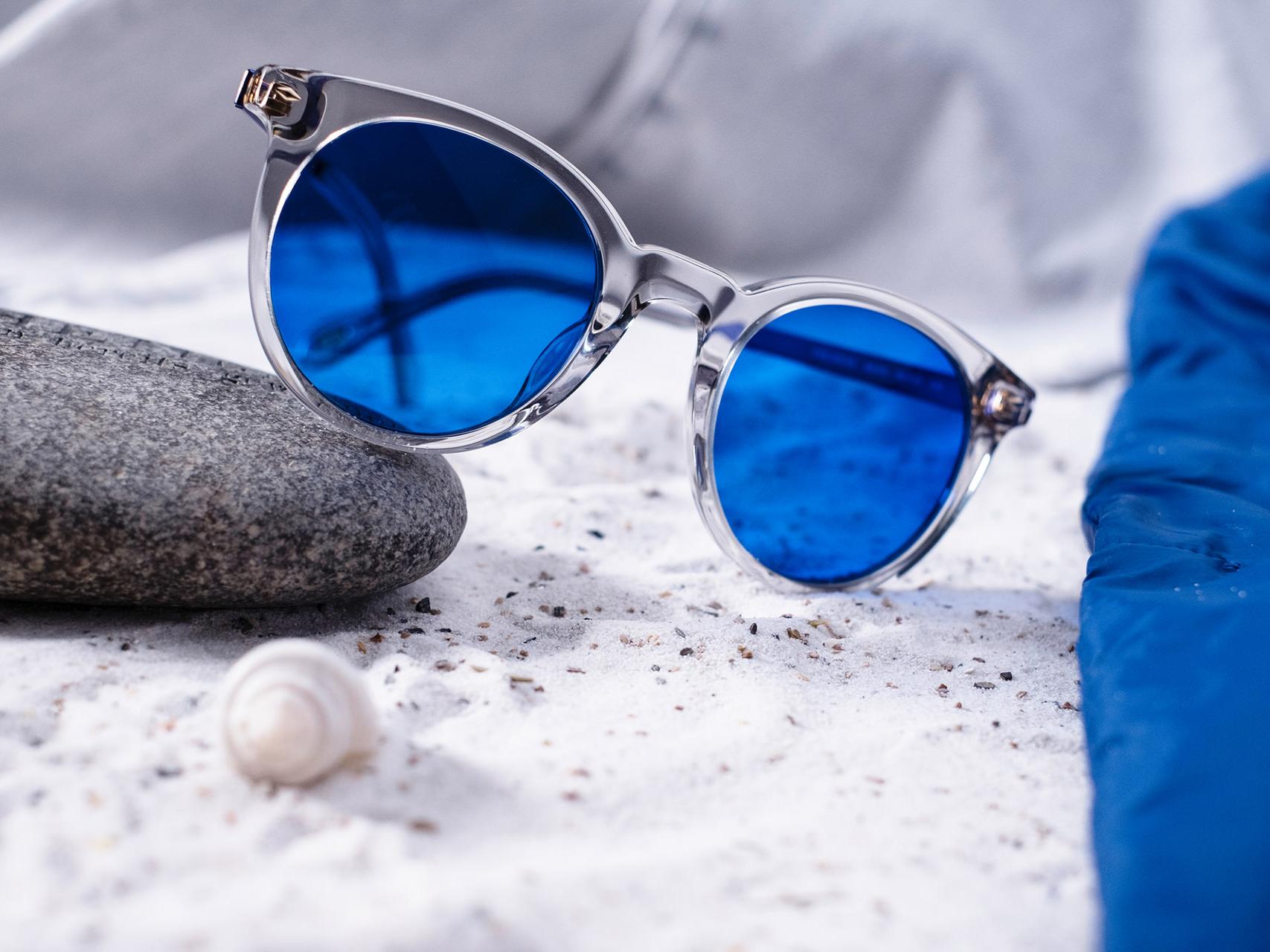 Bild på ett par glasögon med blå färg halvt liggande på en sten