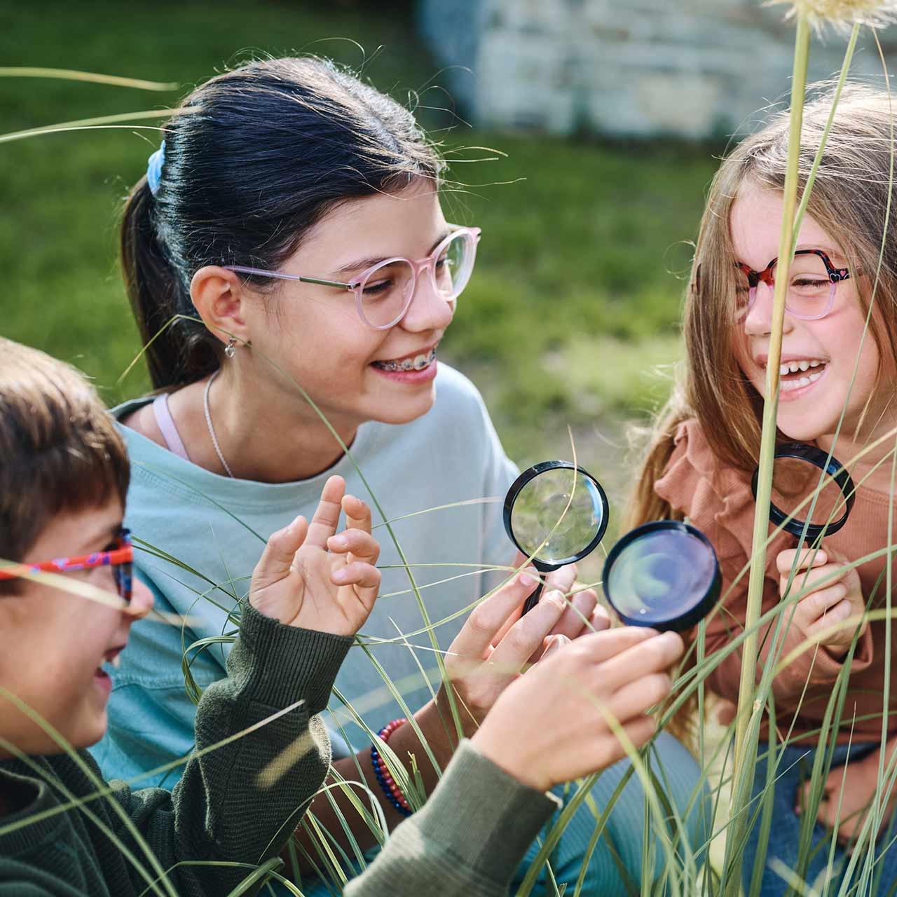 En grupp barn med glasögon och förstoringsglas som leker och skrattar utomhus
