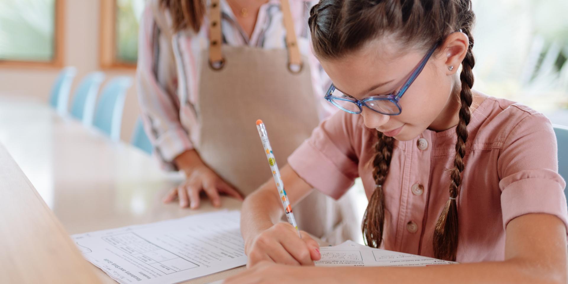 Flicka med glasögon som skriver med en penna