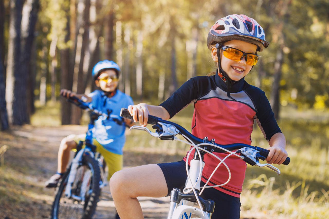 Barn på cyklar i den soliga skogen Barn som cyklar utomhus med hjälm