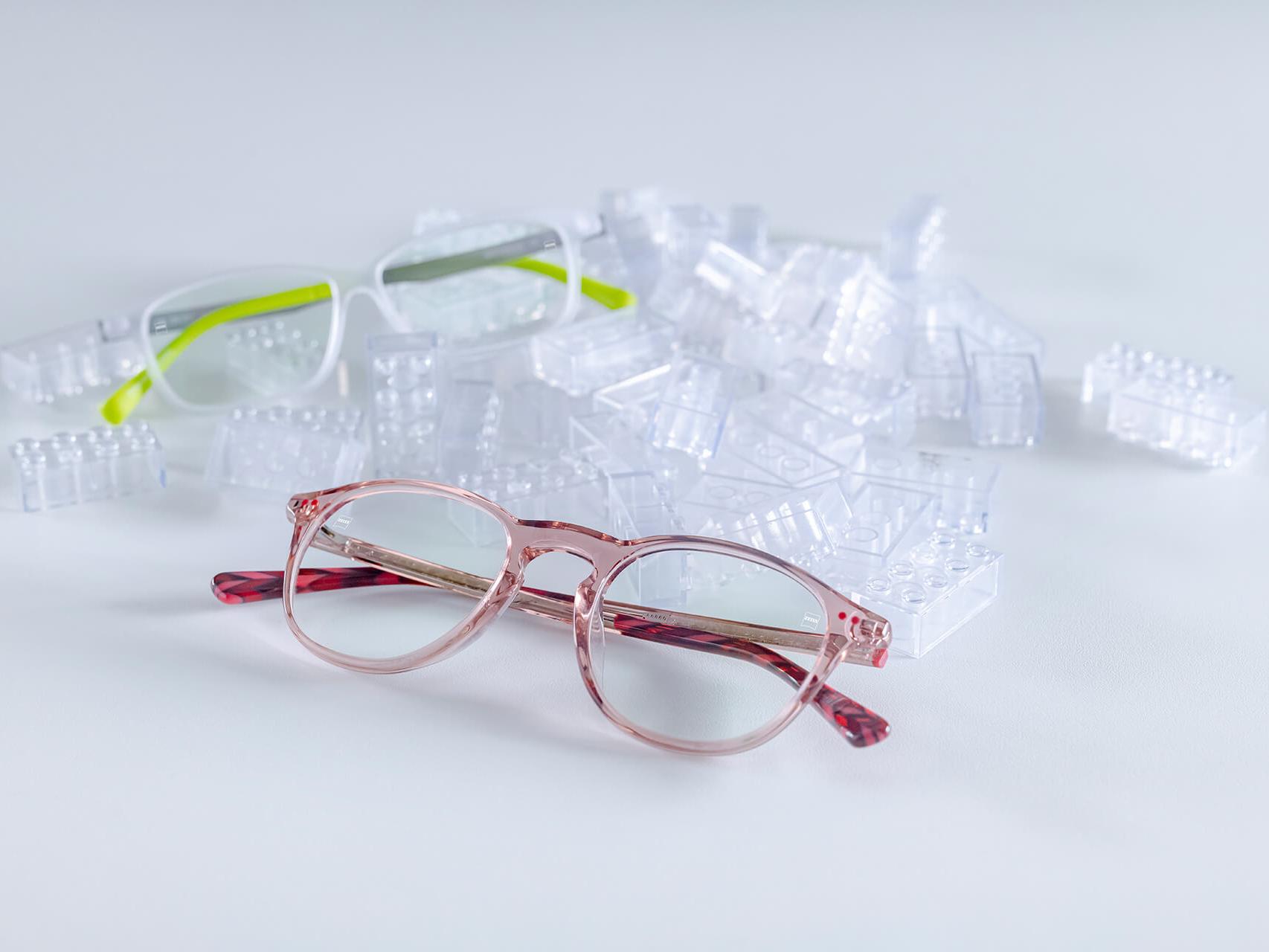 Två par barnglasögon med ZEISS-glas och DuraVision® Kids-ytbehandlingar. Glasögonen ligger bland transparenta lekklossar.