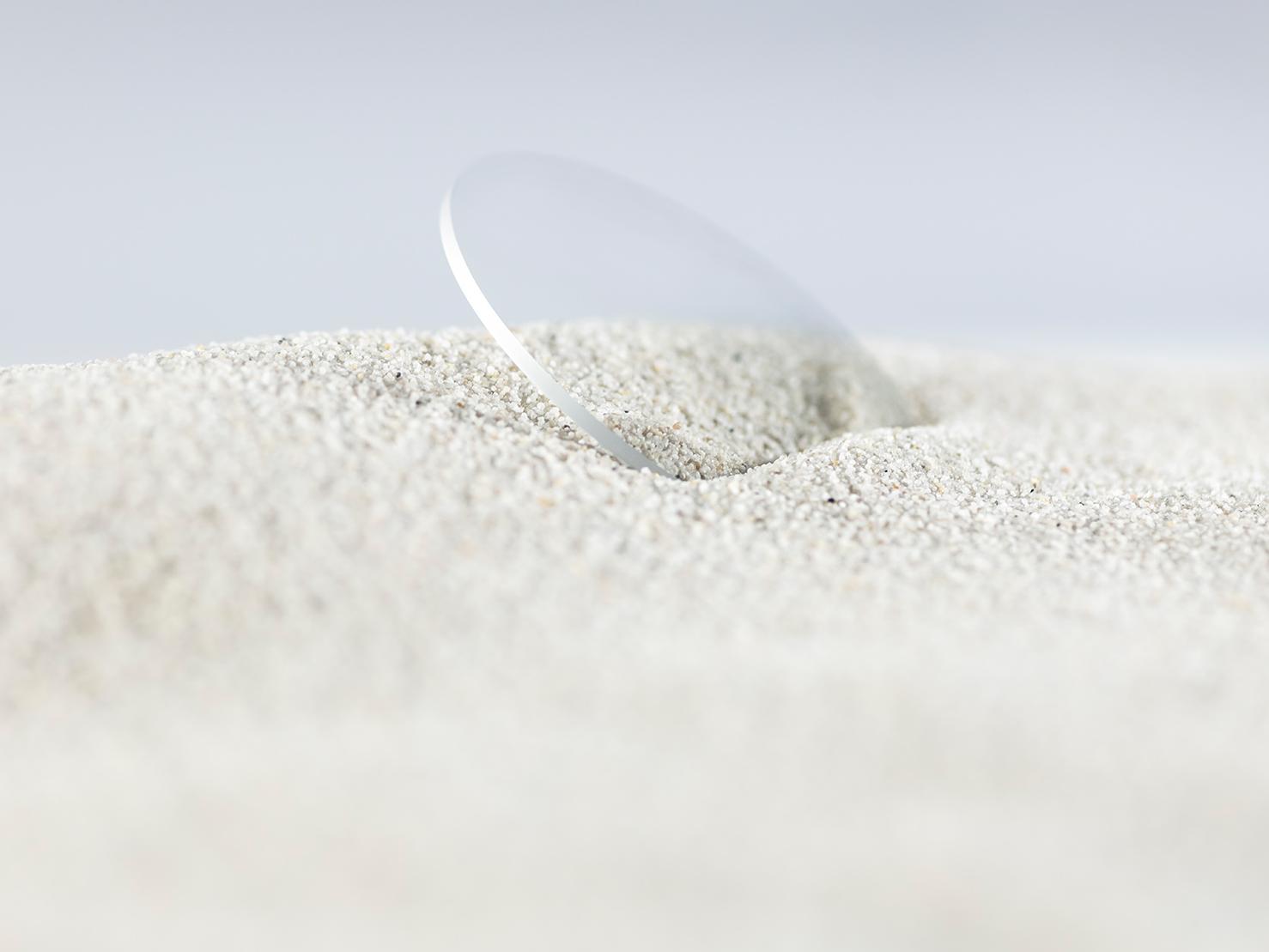 Ett ZEISS-glas med en hållbar ytbehandling är nerstucket i grov sand, men ändå fritt från repor.