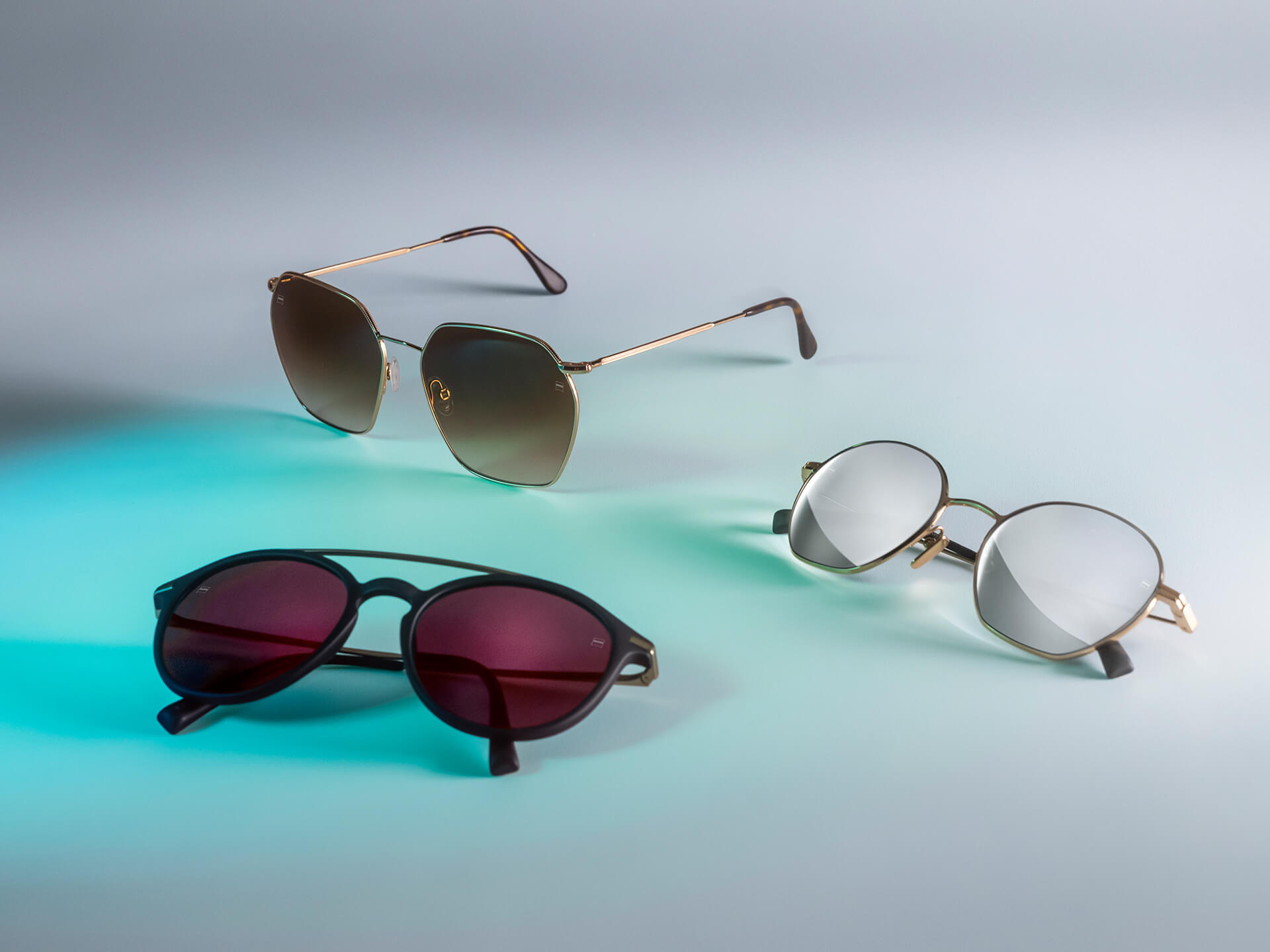 Tre par solglasögon med ZEISS solglas i olika färger, med ytbehandlingarna DuraVision Sun, DuraVision Mirror och Flash Mirror, mot en vit bakgrund med ljusblå reflexer.