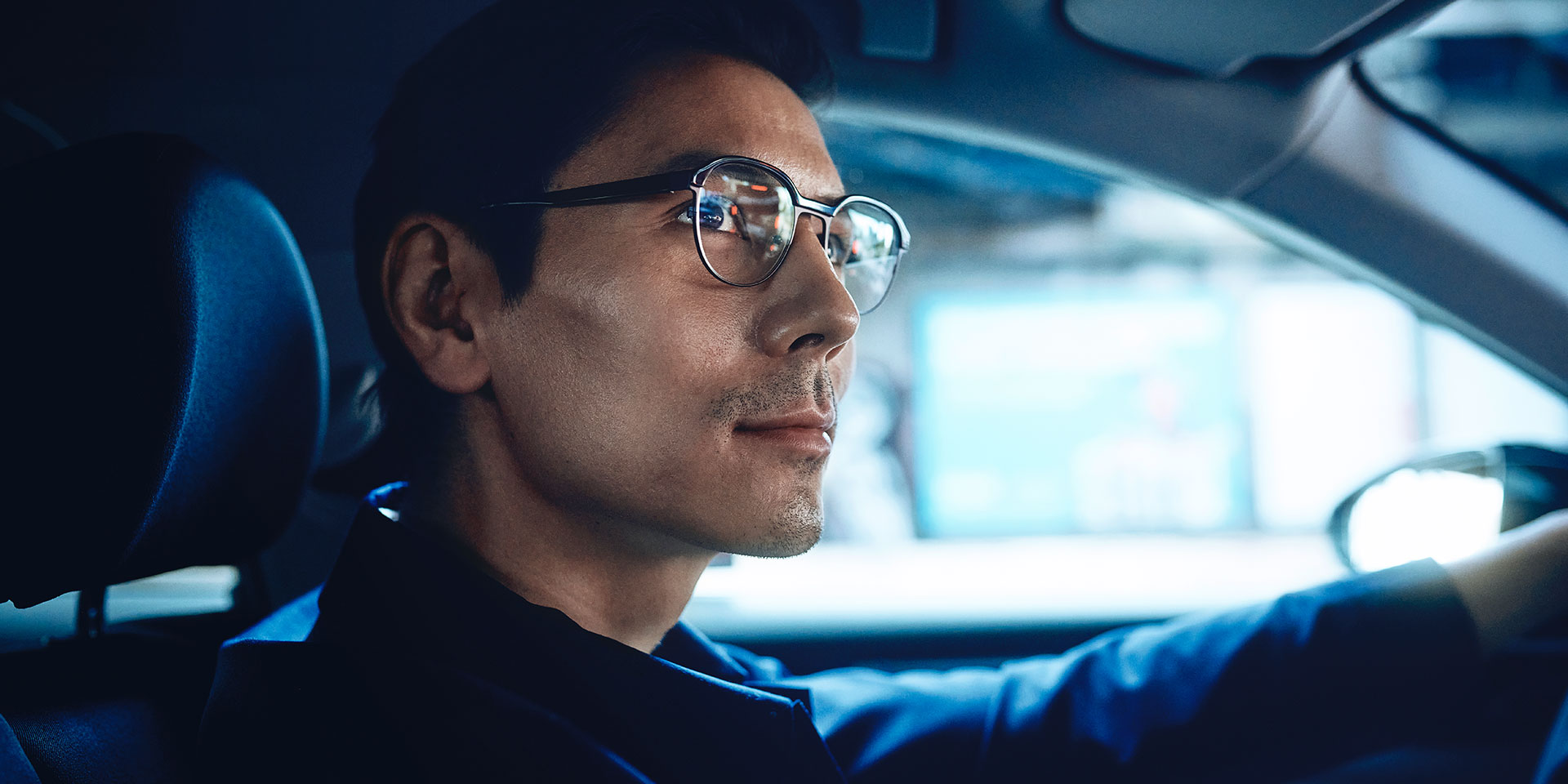 En man kör bil, med ett litet leende på läpparna. Han använder ZEISS DriveSafe enstyrkeglas.