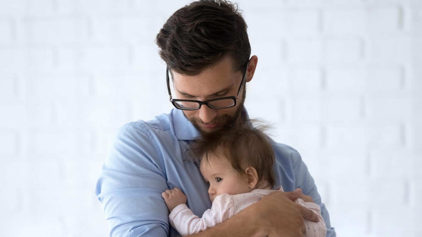 En närsynt man med glasögon håller i ett spädbarn.