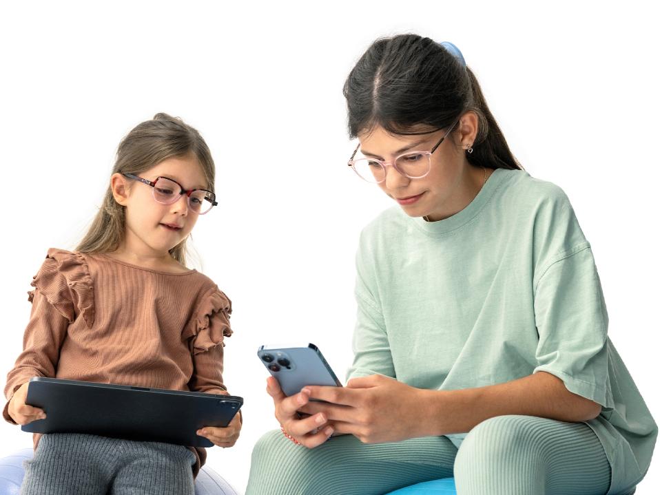 Två flickor tittar på digitala enheter från det rekommenderade avståndet på mer än 20 cm.