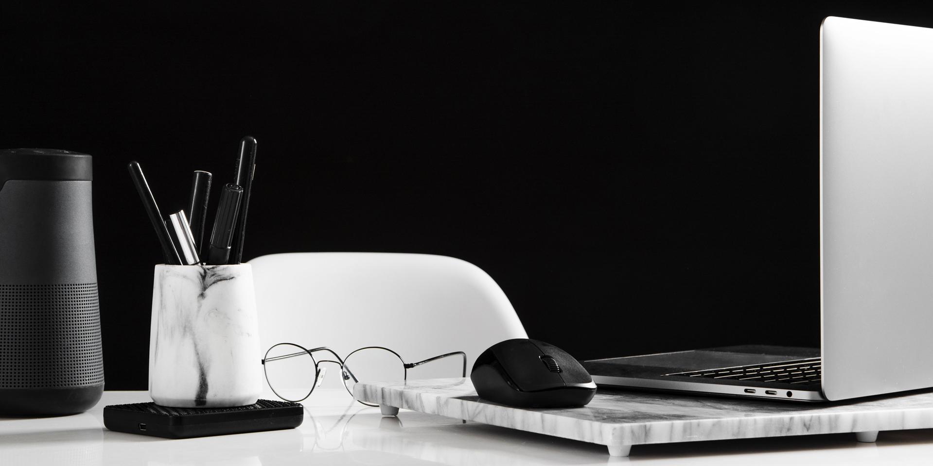 Välstädat skrivbord med en öppnad dator till höger med en mus. Framför den ligger ett par glasögon. Till vänster i bilden står ett pennställ.
