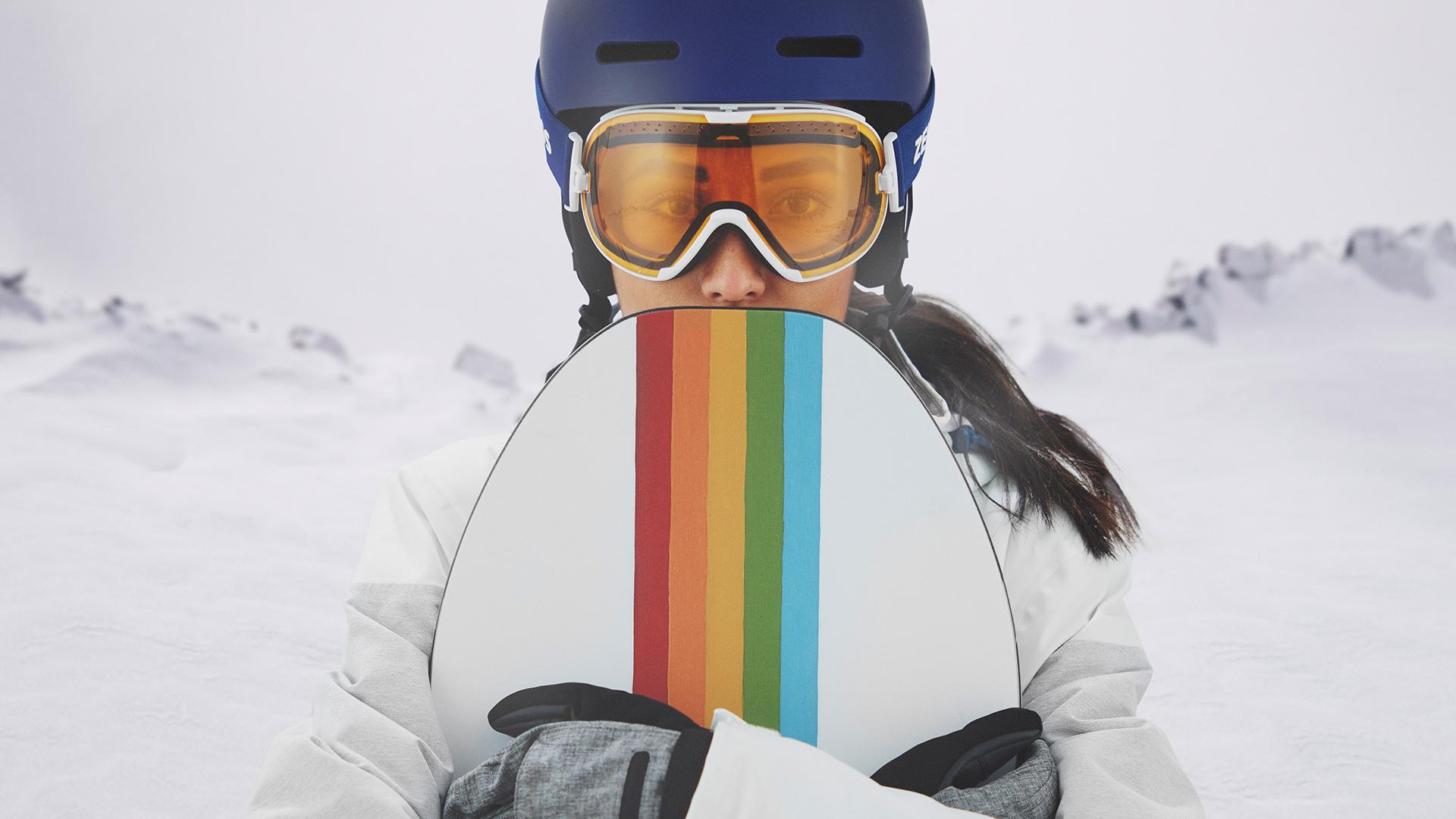 En ung kvinna bär skidglasögon med ZEISS utbytbara linser och håller i en snowboard.