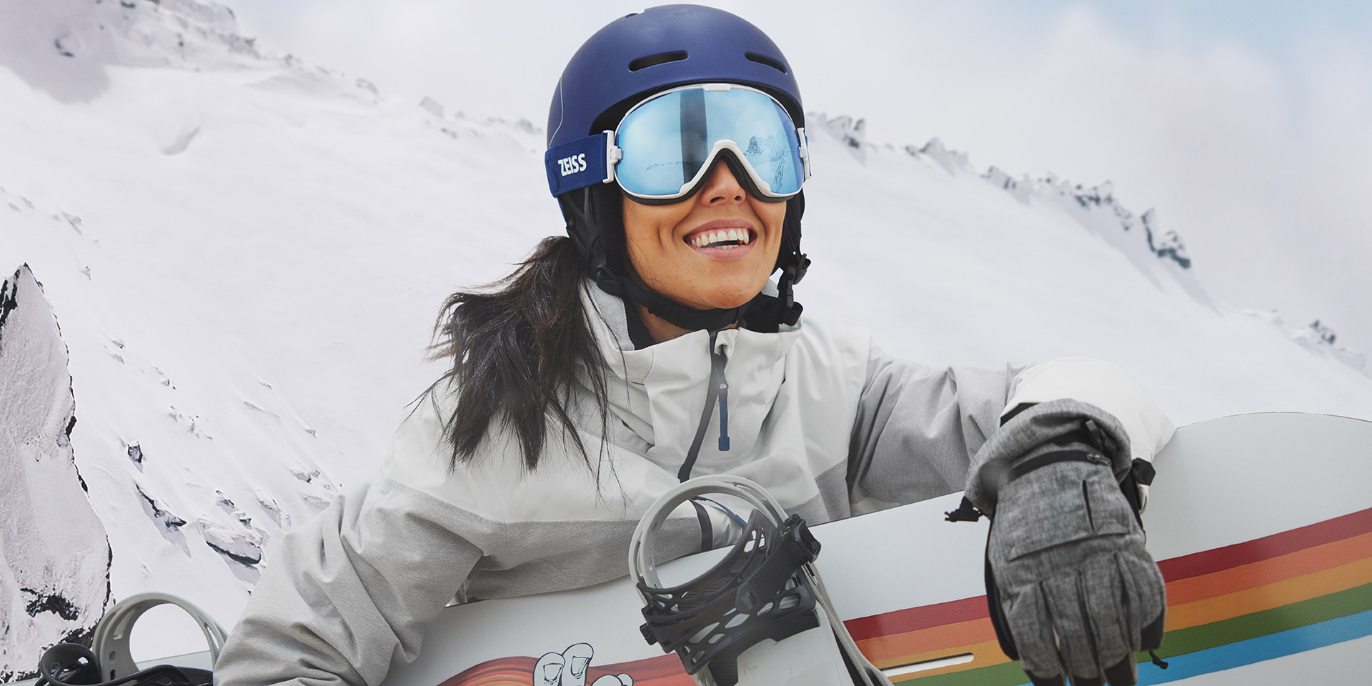 En ung kvinna bär skidglasögon med ZEISS utbytbara linser och håller i en snowboard.