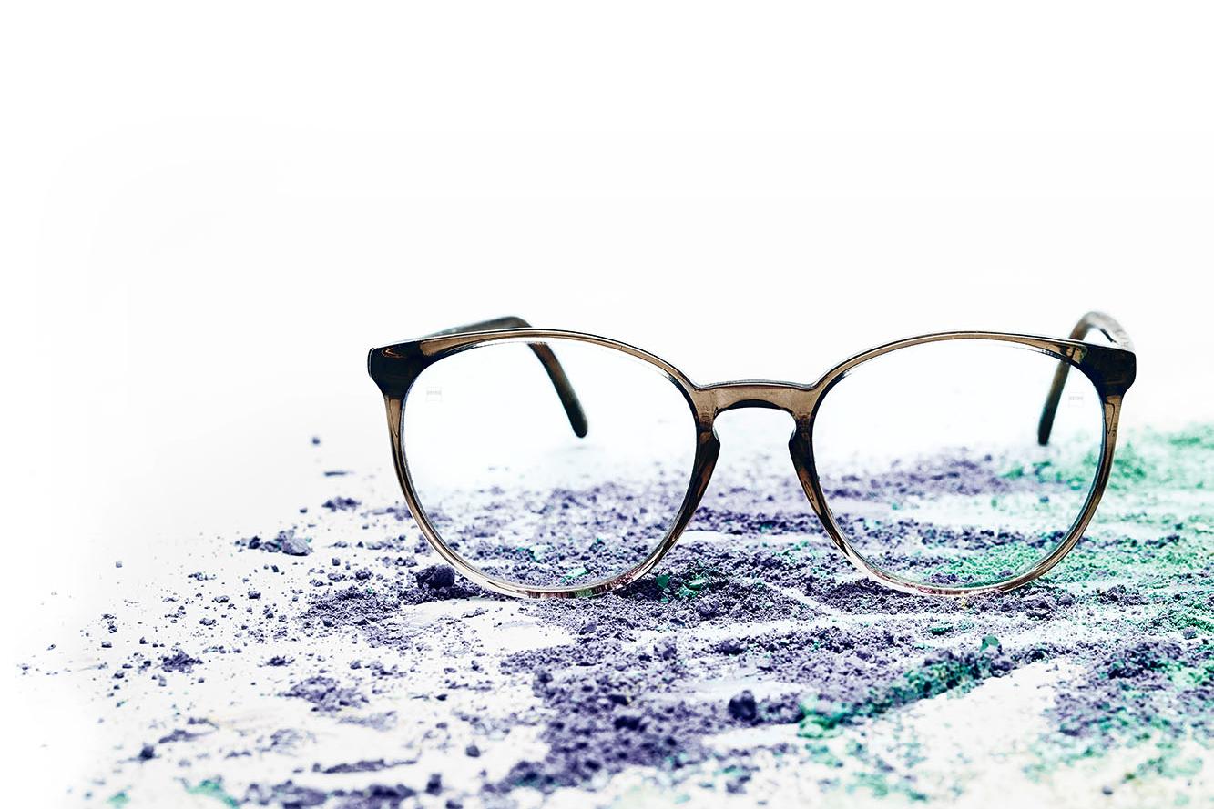 Ett par glasögon med klara glas ligger på ett färgstarkt pulver.
