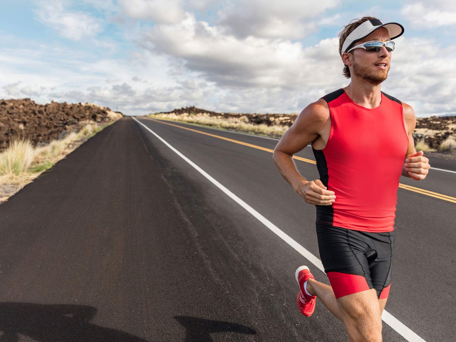 Bild av en man som använder träningskläder och sportglasögon när han springer efter en väg. 