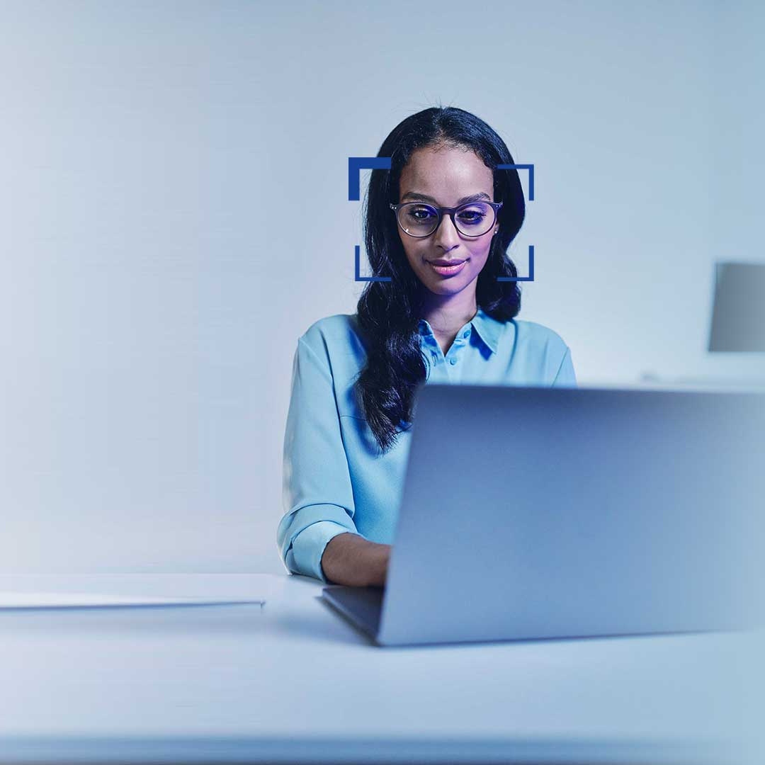 Kvinna med svart hår och glasögon som leende tittar på en bärbar dator