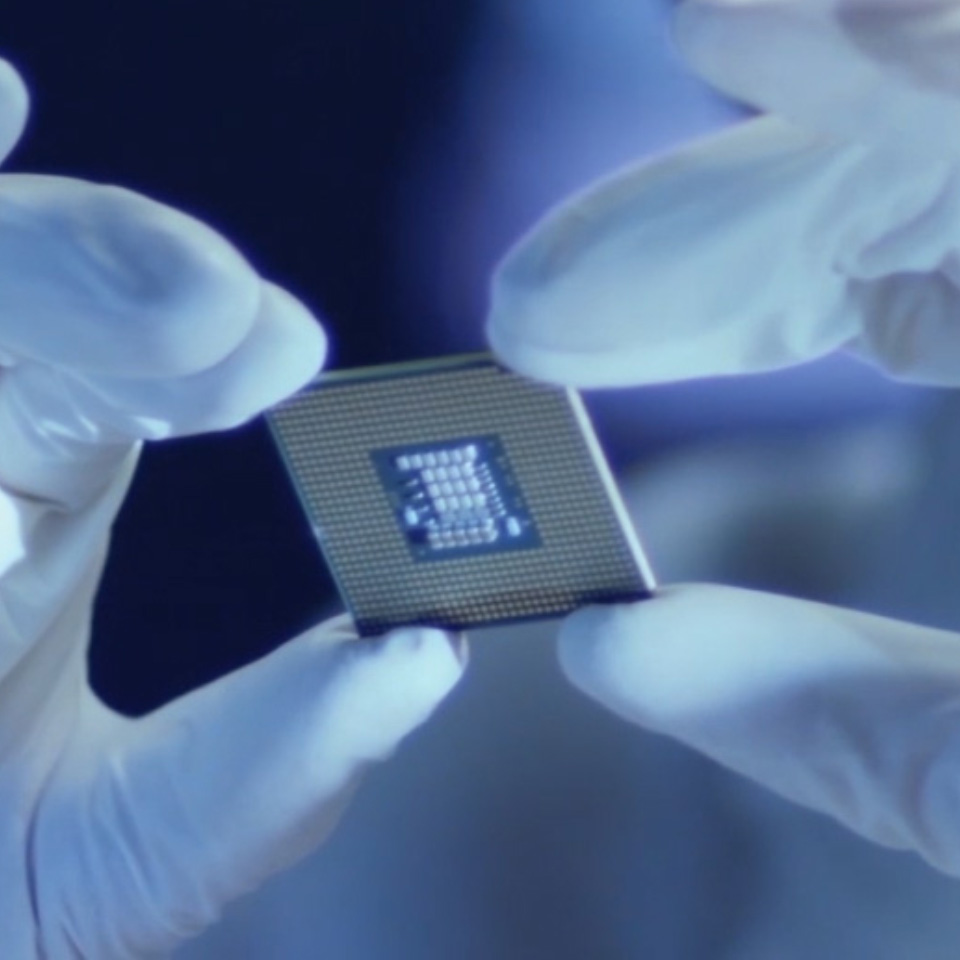 Bild av ett mikrochip som hålls av en person med laboratoriehandskar. 