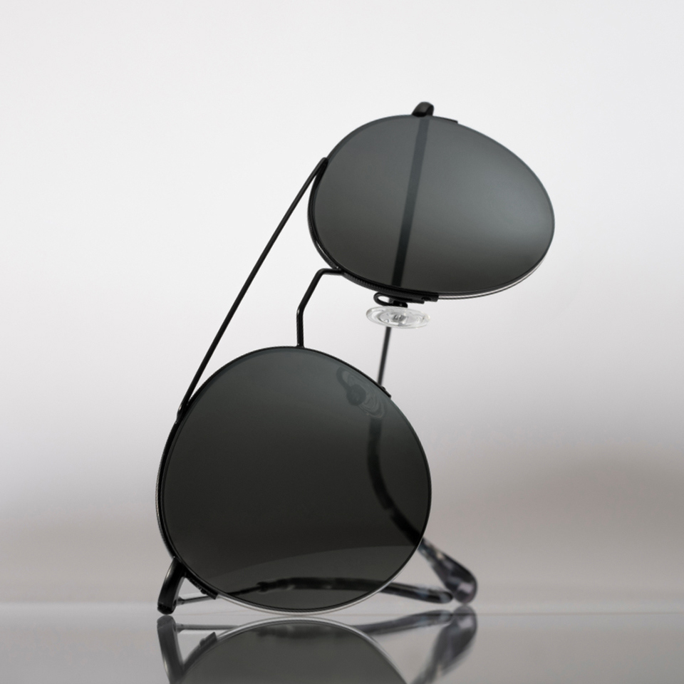 Solglasögon i en grå färg ligger på en ren och ljus yta.