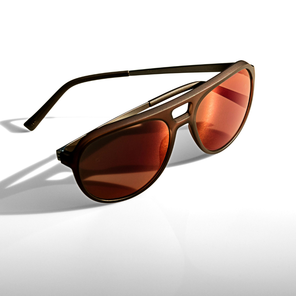 Solglasögon med orange spegeleffekt mot en vit yta och ljus som lyser från sidan.