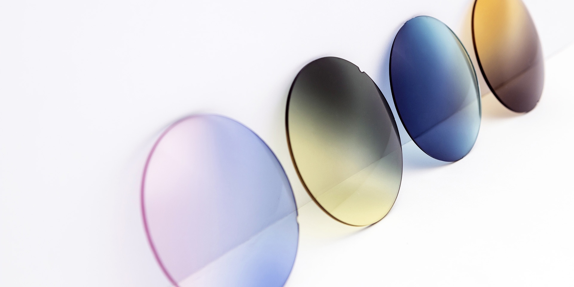 Solglas i olika färger mot en vit yta: rosalila, gulgrå, blå och bruna gradalfärger.
