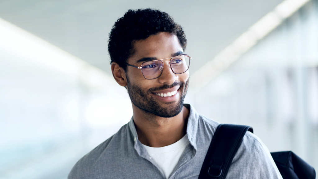 En leende man med en ryggsäck över axeln bär ZEISS Digital SmartLife-glasögon och tittar åt sidan.