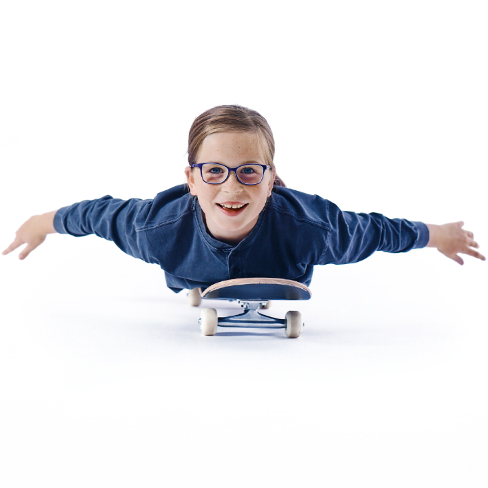 En ung flicka med glasögon ligger på sin skateboard.