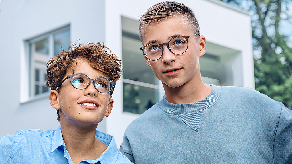 En ung pojke tittar upp mot en något äldre pojke, båda bär enkelslipade ZEISS SmartLife Young-glasögon